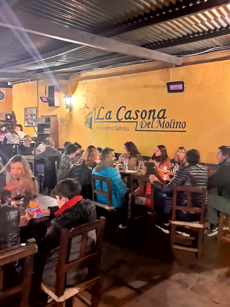 Imagen del interior De la Peña La Casona del Molino, con paredes anaranjadas y personas comiendo y disfrutando de su ambiente animado