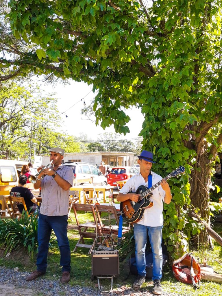 Músicos tocando en vivo, el saxo y la guitarra, en un lugar al aire libre con entorno verde
